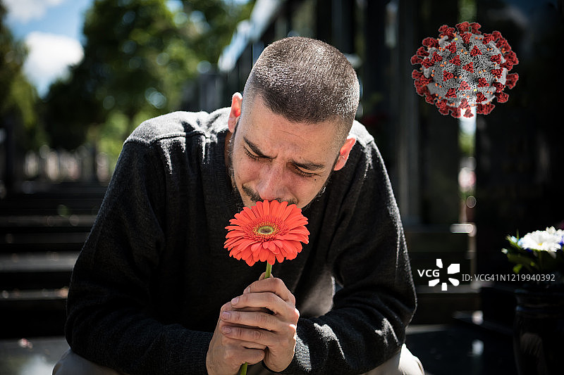 悲伤和沮丧的鳏夫在黑衣跪在墓碑前，拿着一朵花和哀悼家人的损失。死亡、哀悼、葬礼和精神的概念——Covid-19图片素材