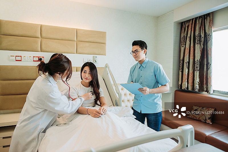 在医院的病房里，亚裔华裔女医生正在用听诊器检查她的女病人图片素材