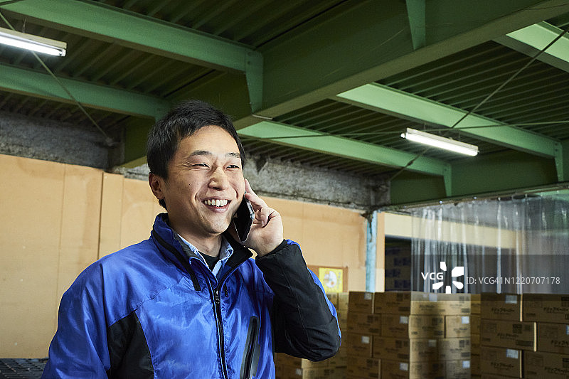 一名日本男性工人在一间仓库里打电话图片素材