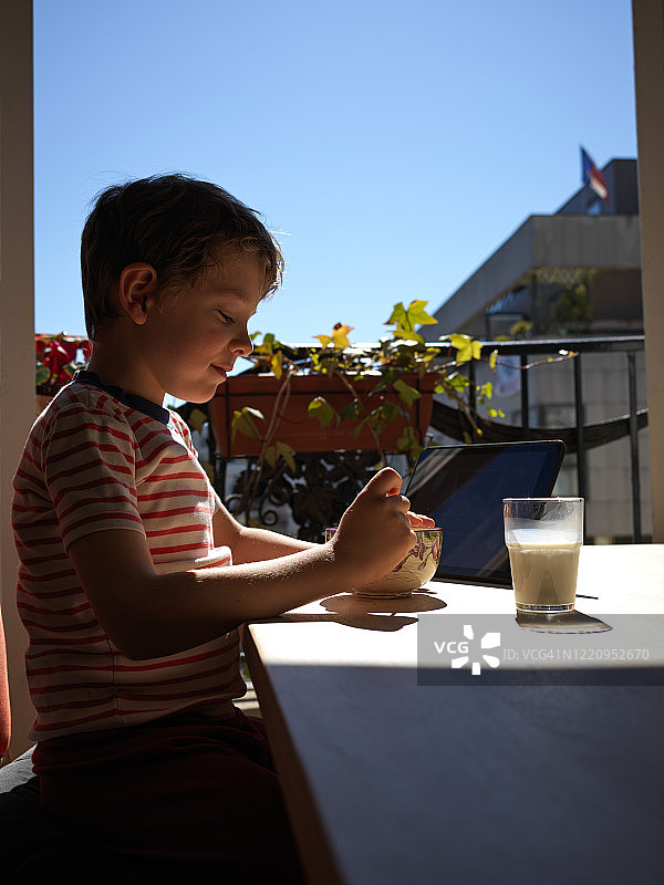 一个小男孩一边吃早餐一边看他的数码平板电脑，早上图片素材
