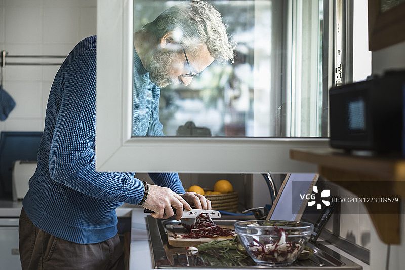 一个成熟的男人在厨房开着的窗户上准备沙拉图片素材