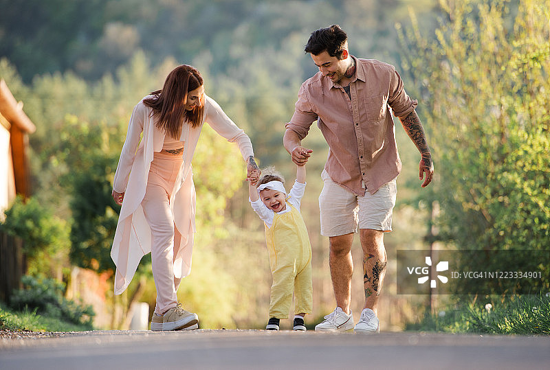一个快乐的年轻家庭和一个蹒跚学步的小女孩在春天的大自然中散步。图片素材