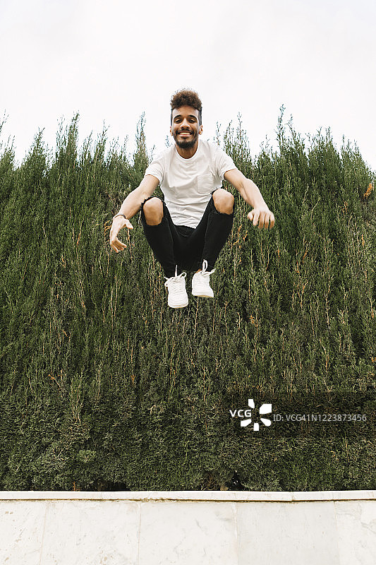 一个快乐的年轻人在户外的空中跳跃的肖像图片素材