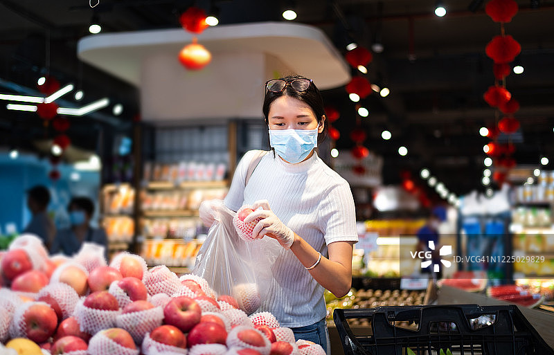 在市场上买水果的亚洲妇女戴着面具和手套图片素材