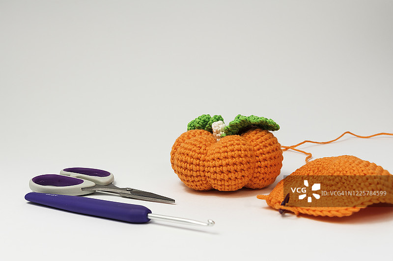特写针织西葫芦与橙色棉线，钩针和剪刀在白色的背景。副本的空间。图片素材