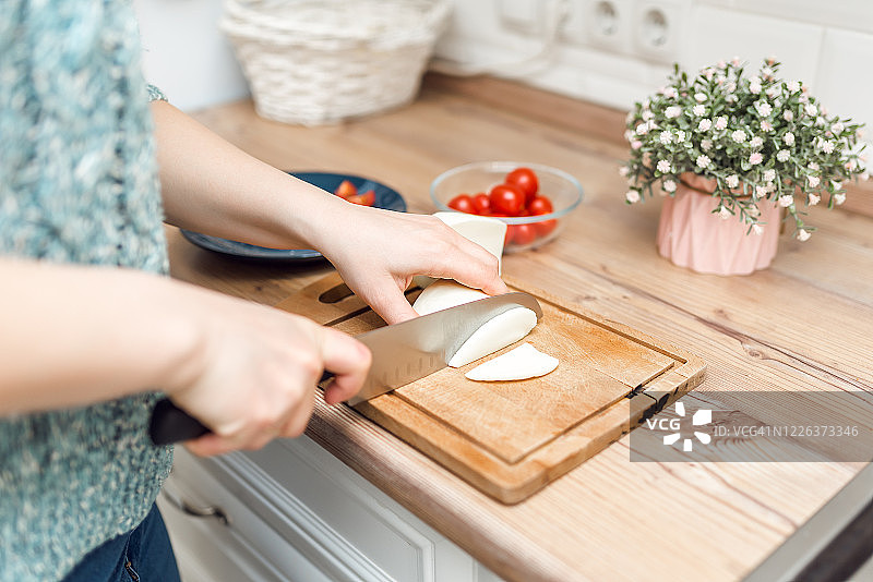 一位穿着蓝色针织毛衣的妇女在厨房的切菜板上切起司。家庭主妇。在自己的厨房里做饭图片素材