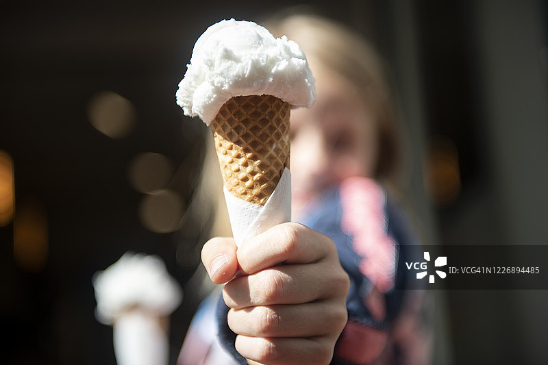 一个八岁的小女孩拿着两个冰淇淋蛋卷，给观众一个图片素材