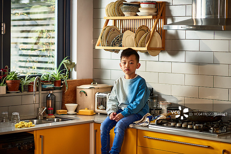 年轻的中国男孩坐在厨房的柜台上图片素材