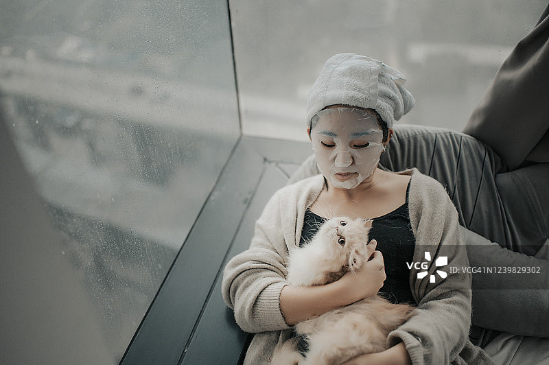 一个亚裔中国少女在卧室里和她的猫做水疗面膜图片素材