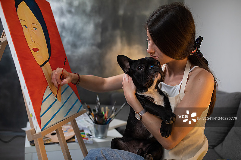 一位年轻漂亮的画家在画画时把下巴搁在她的狗的头上图片素材
