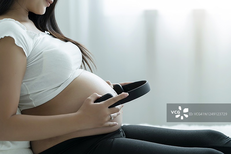 怀孕的西班牙妇女把耳机放在肚子上图片素材