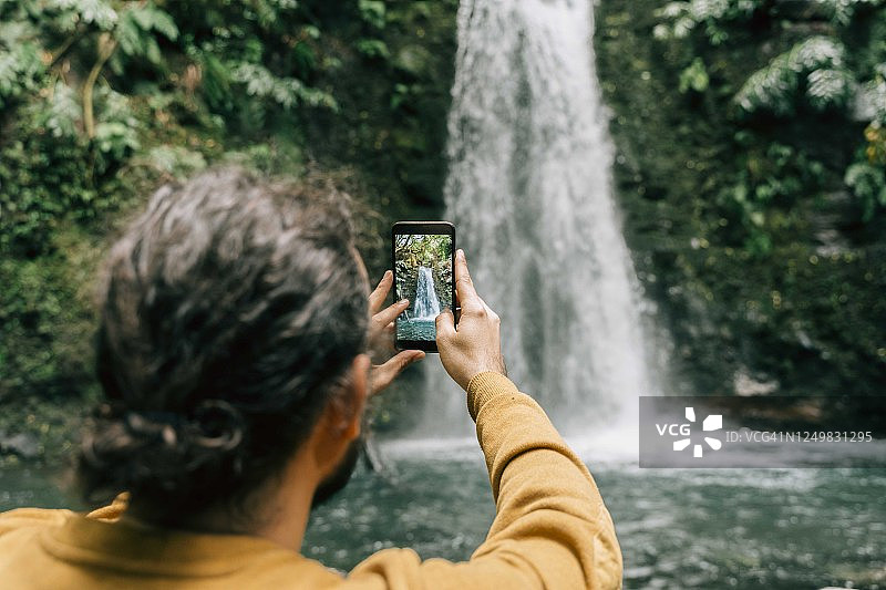 在葡萄牙亚速尔群岛的圣米格尔岛瀑布上拍摄智能手机照片的男人的后视图图片素材