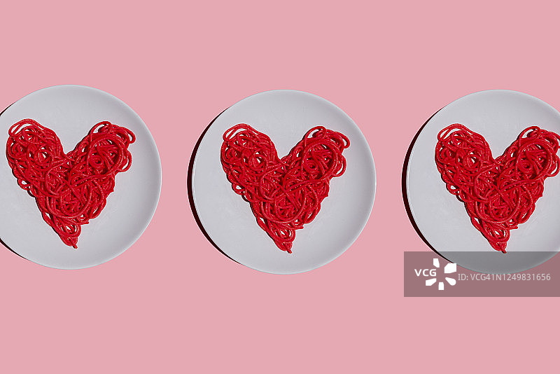 工作室拍摄的三个盘子与红色的心型意大利面在粉红色的背景图片素材