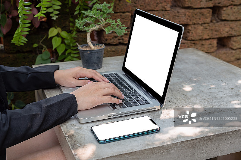 一位在户外花园使用笔记本电脑的亚洲女性。图片素材
