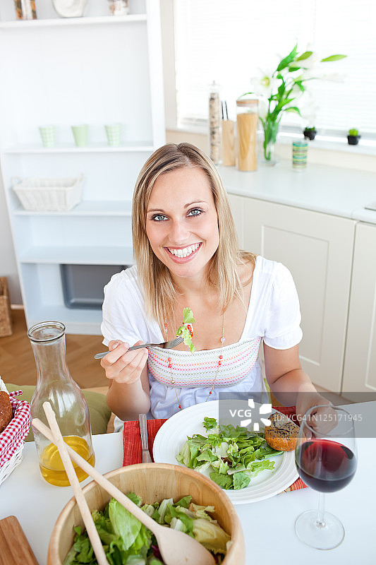 微笑的女人在厨房吃沙拉图片素材