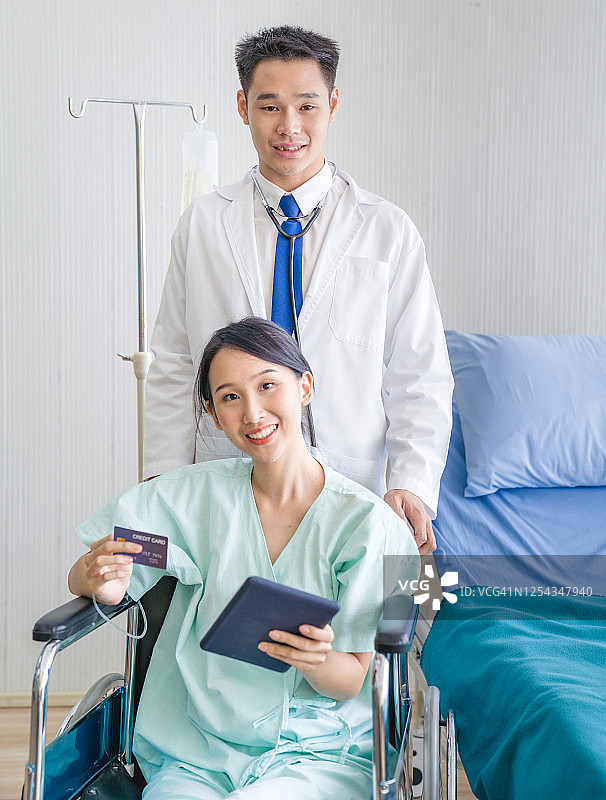 年轻的亚洲女性患者坐在轮椅上在医院使用数字平板电脑和信用卡进行在线支付图片素材