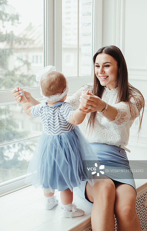 微笑的母亲坐在窗台上和她的宝贝女儿玩耍图片素材