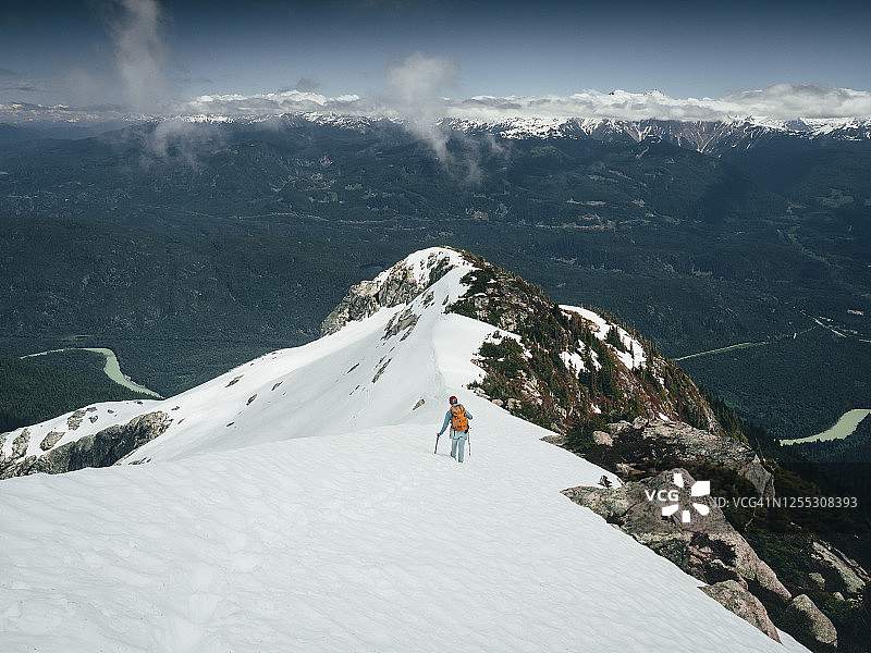 女登山者走下陡峭的，白雪覆盖的山脊高在森林山谷下面图片素材