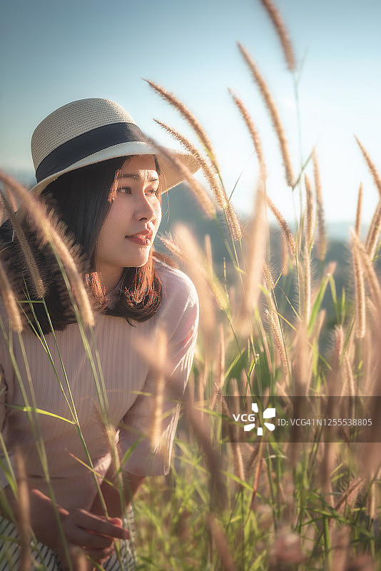肖像美丽的女人在时尚的帽子，而享受在草地在日落。图片素材