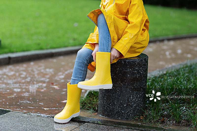 可爱的小女孩穿着黄色雨衣和胶靴在雨中户外散步。天气恶劣，夏季热带风暴，秋季时尚概念图片素材