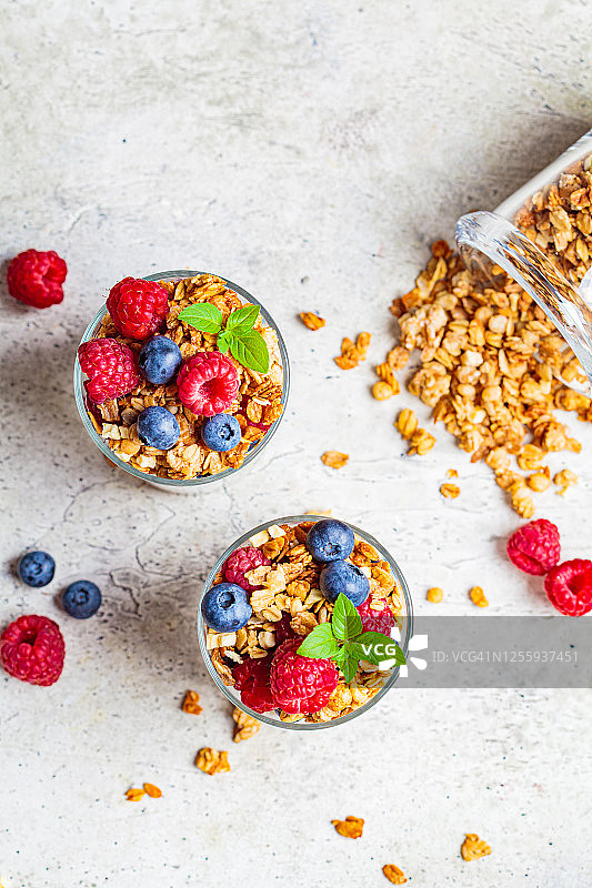 酸奶冻配格兰诺拉麦片，覆盆子和蓝莓，浅灰色背景，俯视图。健康的早餐概念。图片素材