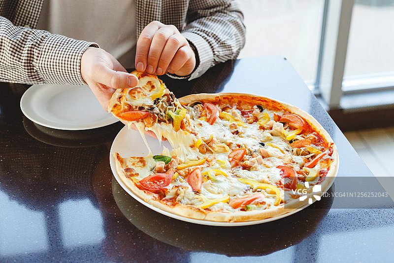 美味的披萨外卖。一名白种人在咖啡馆、餐馆或家里拿着一块美味的意大利披萨，上面有马苏里拉奶酪。快餐披萨外卖。图片素材