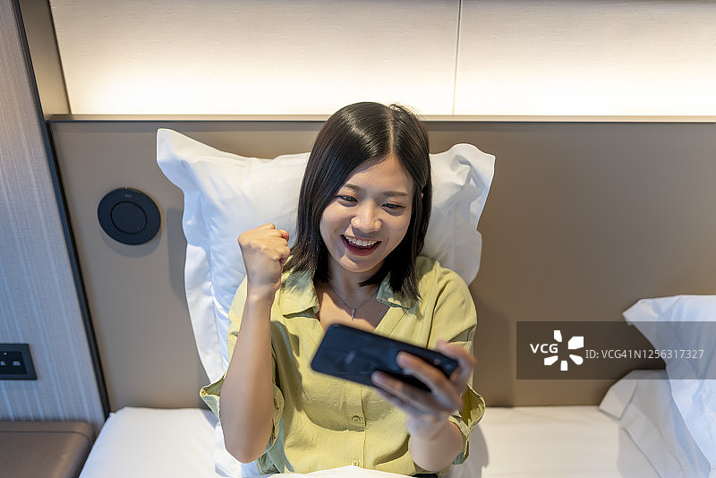 一个亚洲女人在床上玩电子游戏图片素材