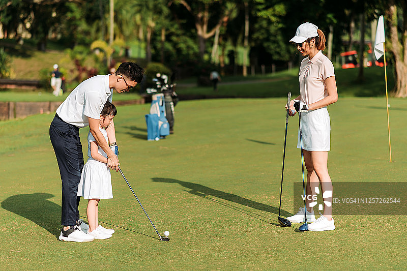 年轻的亚洲华人父母在高尔夫球场教女儿打高尔夫球图片素材