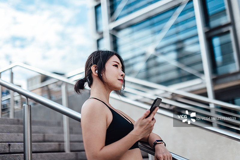 年轻的亚洲女性跑步者在休息时使用智能手机图片素材