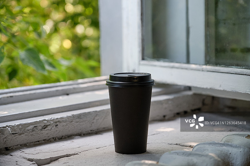 一个一次性的咖啡杯或杯子放在开着窗户的木窗台上。图片素材