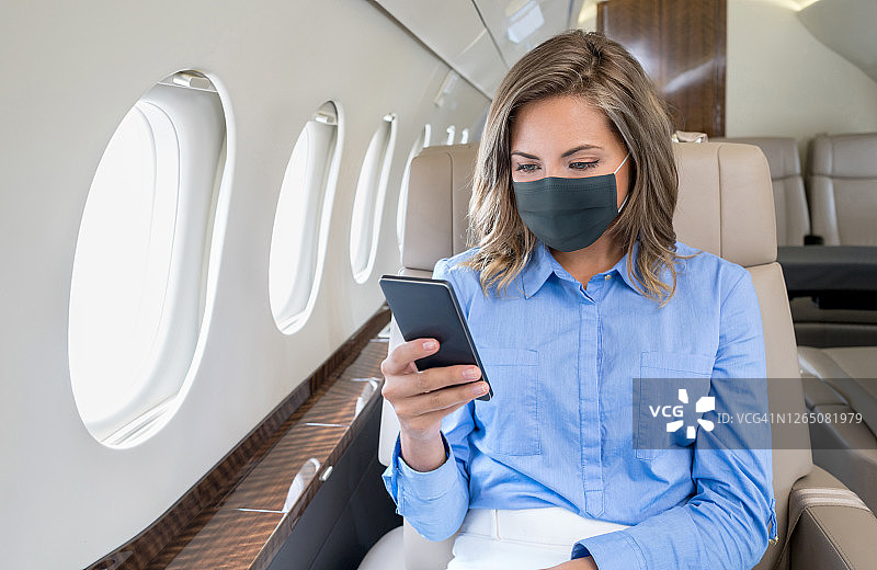 商务女性乘坐私人飞机时戴着口罩并使用手机图片素材