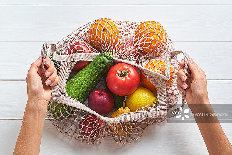 新鲜多汁的水果和蔬菜，产品在一个可重复使用的购物袋。白色背景的女孩或妇女手中用可回收材料制成的网袋。素食主义，纯素食主义，生食饮食。没有塑料。图片素材