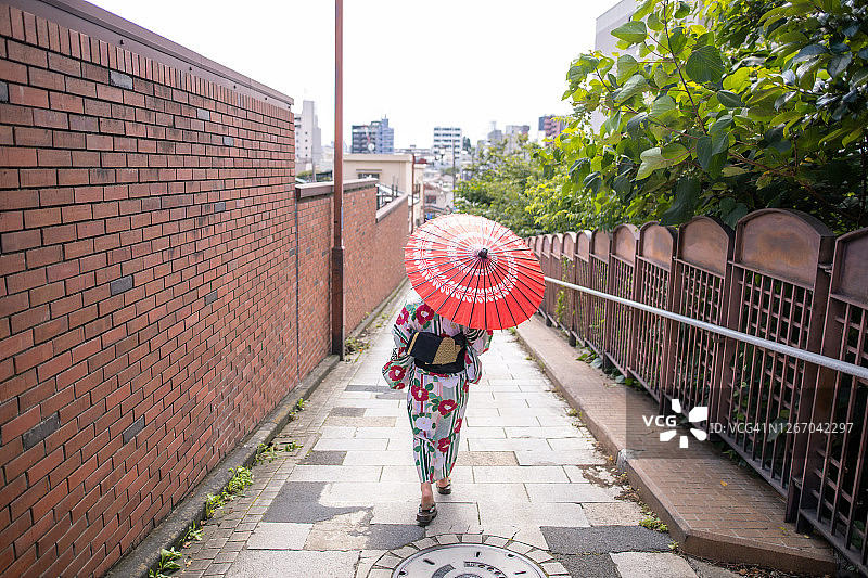 浴田的一名年轻女子拿着红纸伞从山坡上走下来图片素材