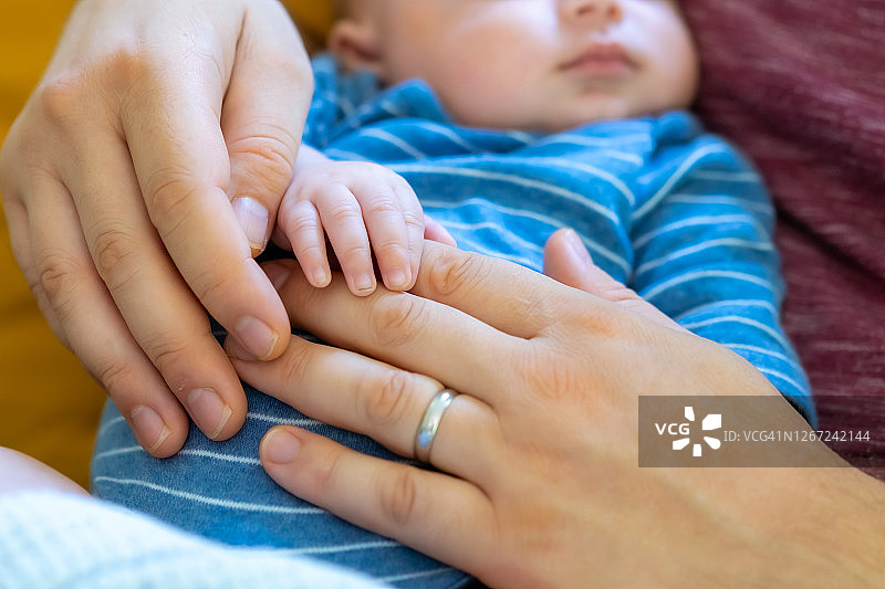 白人家庭的父亲和母亲与他们可爱的新生儿儿子是手拉着手一起睡觉的特写。妈妈抱着一个男婴。幸福家庭，宝宝保健理念。图片素材
