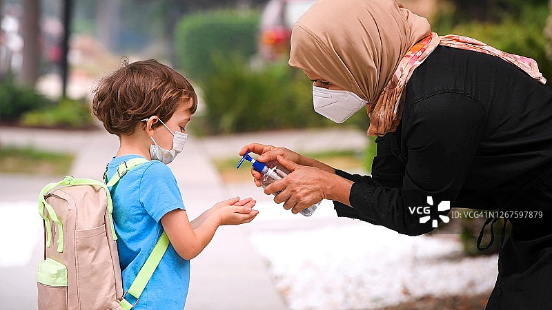 一名穆斯林母亲在儿子回学校之前往他手上浇消毒剂图片素材