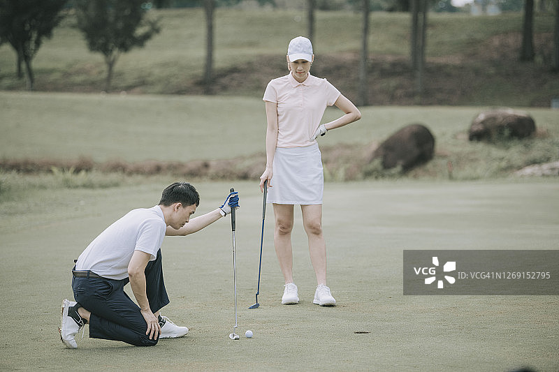 亚洲华人男子高尔夫球手与他的同伴在高尔夫球场的高尔夫洞附近排列高尔夫球图片素材