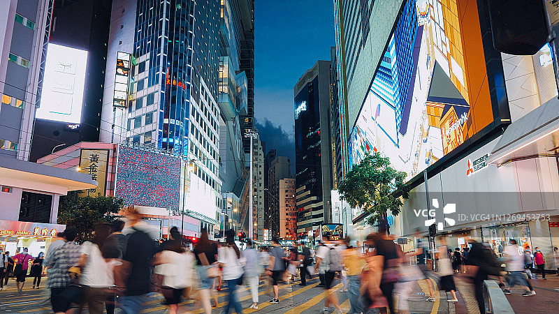 典型的香港城市生活。在交通高峰时间，一群忙碌的通勤者在市中心街道上模糊的移动，在夜色中，城市建筑的灯光和五颜六色的广告牌和商业标志图片素材