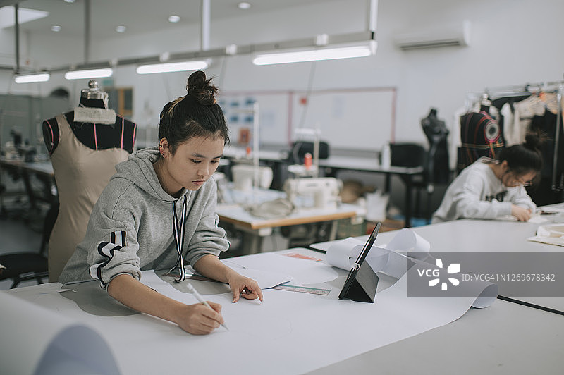亚裔华裔时装女大学生，在学院工作室做服装项目，记录尺寸，绘制缝纫图案图片素材