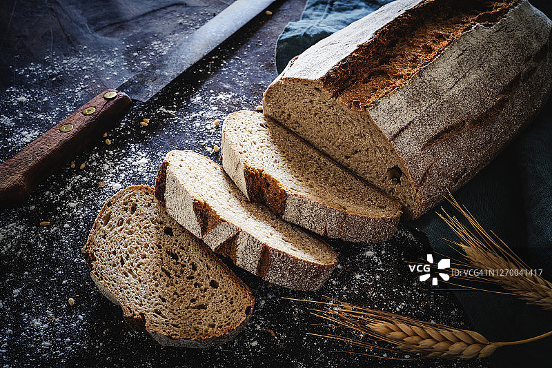 全谷物黑麦面包条，用老式的小刀盖在深色的木头上图片素材