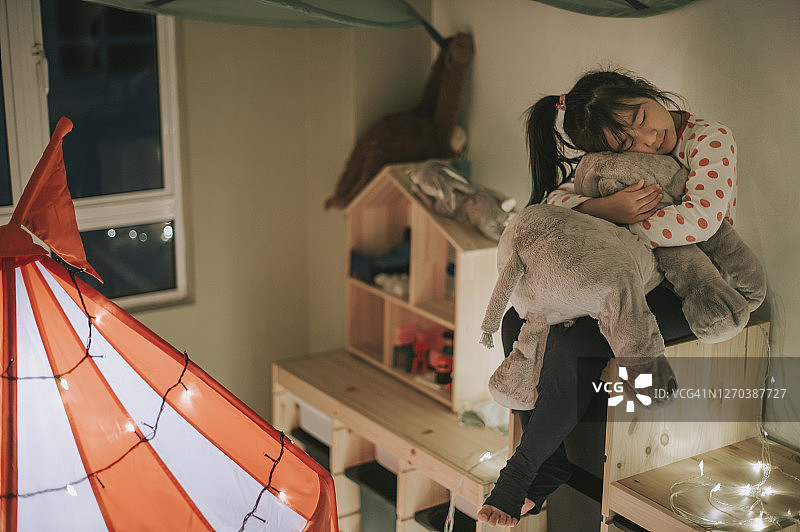 亚裔华人孩子在帐篷里的游戏室里玩，抱着一个放在柜子上的毛绒玩具图片素材