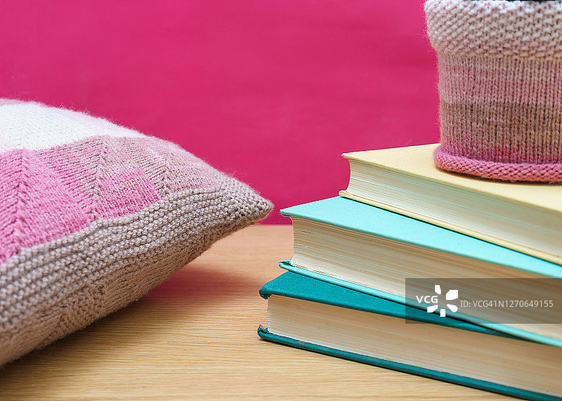一堆旧书放在一个木制书架上，粉红色的背景和针织装饰枕头。家居装饰图片素材