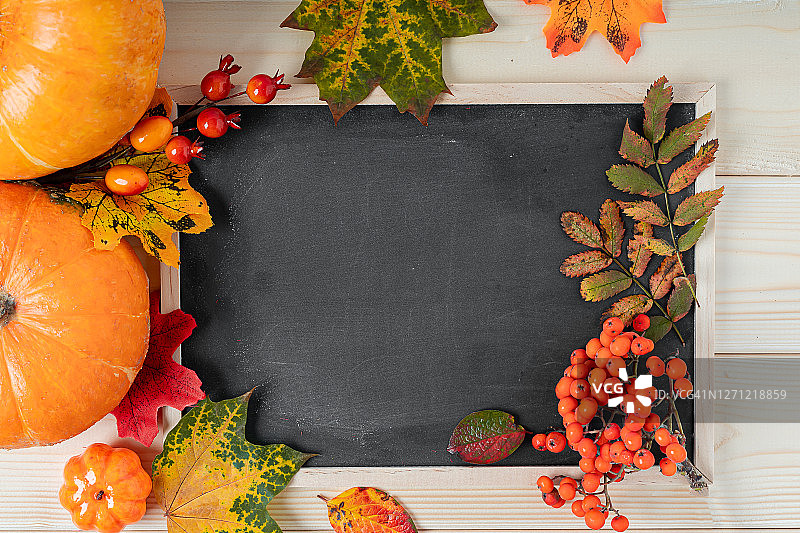 南瓜，浆果和落叶与粉笔模拟黑板框架在木制的背景。为文本复制空间。万圣节、感恩节或秋季季节。平铺，俯视图设计图片素材