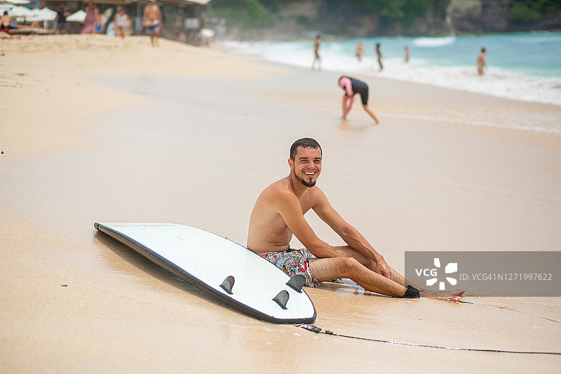 在冲浪后，这家伙正在热带沙滩上休息。健康积极的生活方式在暑假图片素材