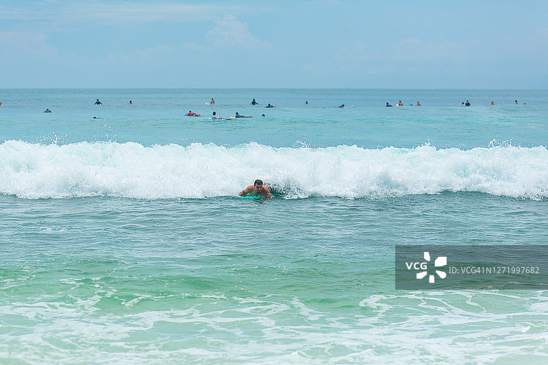 这家伙在海里冲浪板上游泳。健康积极的生活方式在暑假。图片素材