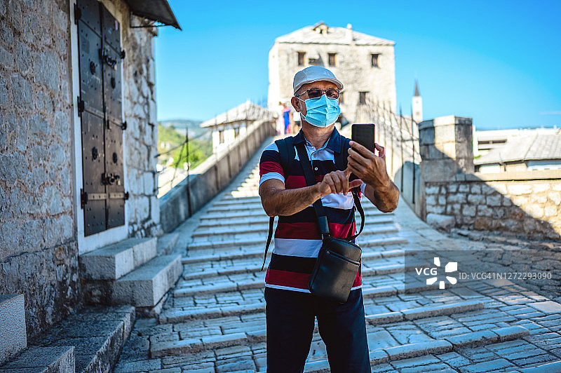 波斯尼亚和黑塞哥维那，成年男性游客戴着保护面罩在莫斯塔尔的老桥上自拍。图片素材