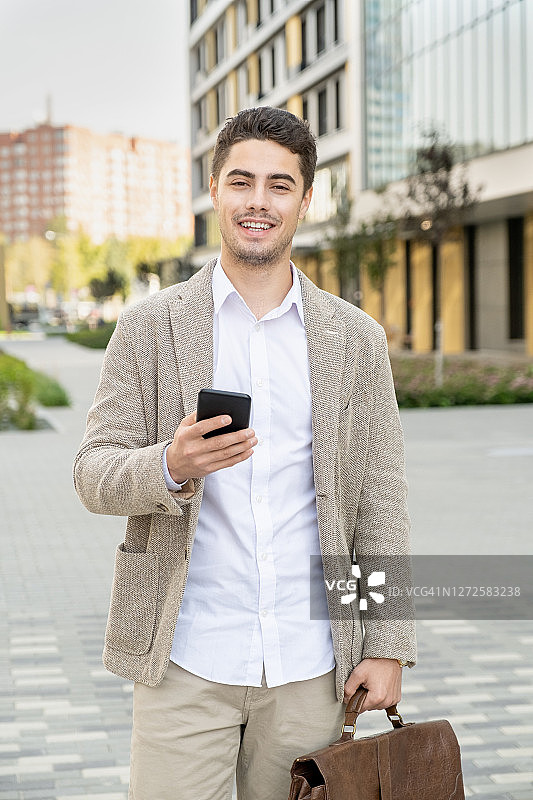 开朗的年轻商人穿着时髦的休闲装在户外使用手机图片素材