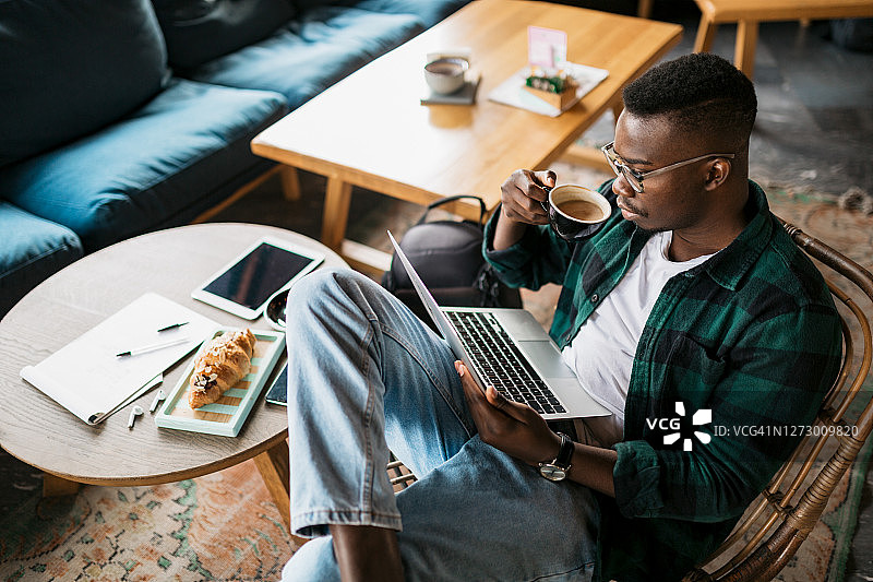 一个年轻的非裔美国人在一家咖啡馆的网上工作的高角度视图图片素材