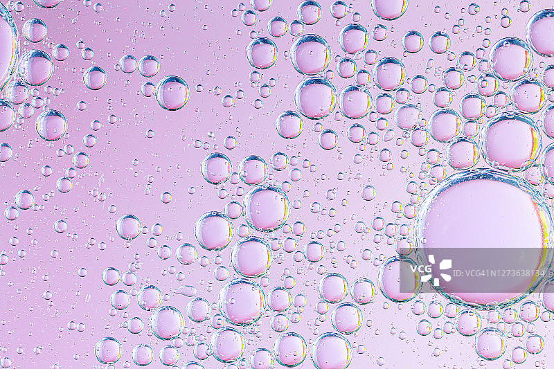 特写抽象气泡油在水与粉色光泽的背景，微距图像，液滴模糊，甜美的颜色图片素材