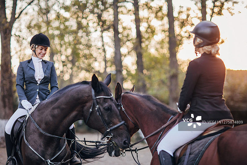 马与两个年轻的女骑手在户外马术竞技场相遇图片素材