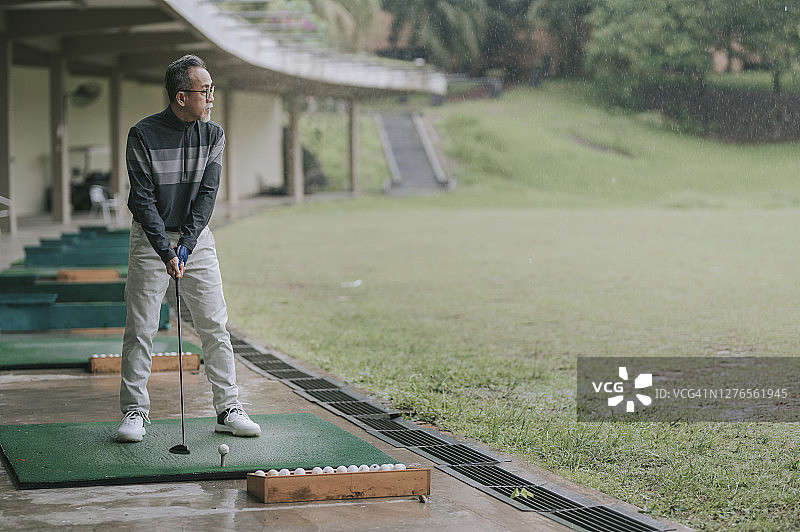 亚洲华人活跃的高级男子高尔夫球手在高尔夫练习场开球和挥杆他的潜水高尔夫球杆图片素材